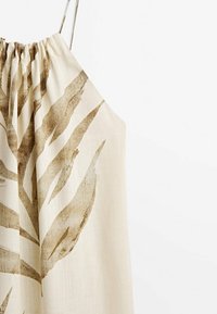 Robe sans manches couleur crème avec fines bretelles et grand imprimé feuille marron sur le devant.