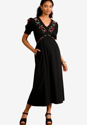 Abito maxi nero con ricami floreali sul corpetto, maniche a sbuffo corte e tasche laterali. Tessuto morbido con una finitura strutturata.