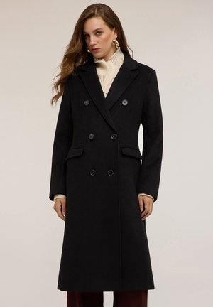 Cappotto doppiopetto nero in misto lana, caratterizzato da revers a scalpello, due tasche frontali e grandi bottoni neri; lunghezza media con vestibilità sartoriale.