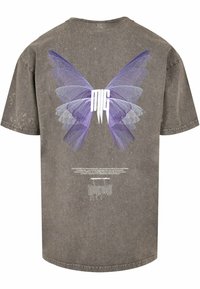 Grå oversized t-shirt med et stort lilla sommerfuglegrafik på ryggen og hvid tekst nedenfor. Blødt, struktureret stof med et falmet look.