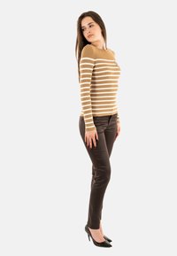 Maglietta a maniche lunghe marrone a coste con righe bianche, abbinata a pantaloni attillati marroni scuri e scarpe col tacco nere. La modella è in posa di profilo.