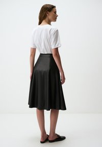 Jupe midi en similicuir noir avec un design évasé, une texture lisse et une taille haute. Assortie à un t-shirt en coton blanc et des chaussures noires à enfiler.