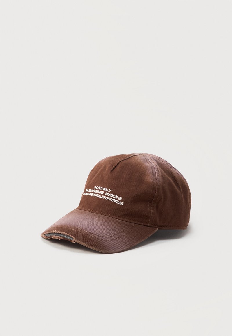 Καφέ φθαρμένο καπέλο μπέιζμπολ με μικρό λευκό τυπωμένο κείμενο μπροστά και ξεφτισμένη άκρη στο γείσο, σε απλό φωτεινό φόντο.