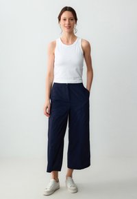 Witte geribbelde tanktop, marineblauwe wijde broek met zakken en witte sneakers. Gladde stof, losse pasvorm en casual ontwerp.