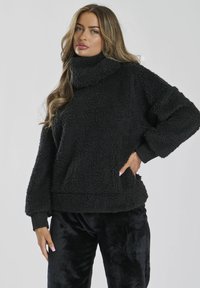 Pullover in pile nero con colletto alto e maniche lunghe. Presenta una superficie morbida e testurizzata, abbinato a pantaloni di velluto neri.