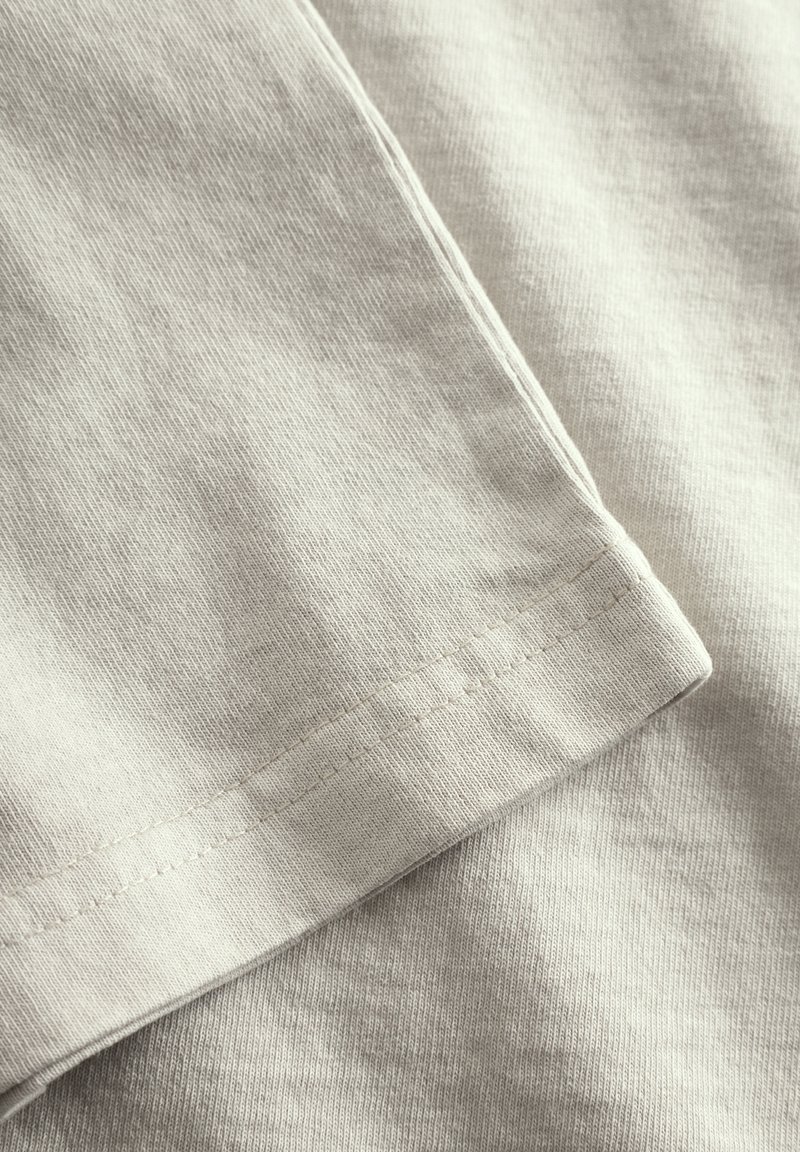 Tissu en coton beige clair avec une texture lisse, présentant un motif de tricot visible et des coutures propres doublement piquées le long des bords.