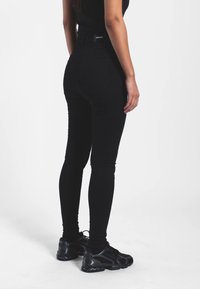 Černé skinny džíny s vysokým pasem a přiléhavým střihem, vyrobené z texturované látky a se malou logovou cedulkou na pase.