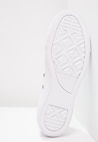 Sole of a white Converse All Star sneaker showing textured tread pattern and brand logo facing upward on a white surface.