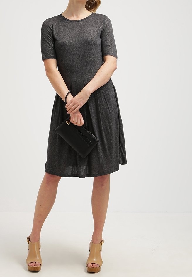 Robe grise à manches courtes avec un col rond, une jupe évasée et une texture subtile. Associée à une pochette noire et des sandales compensées beiges.