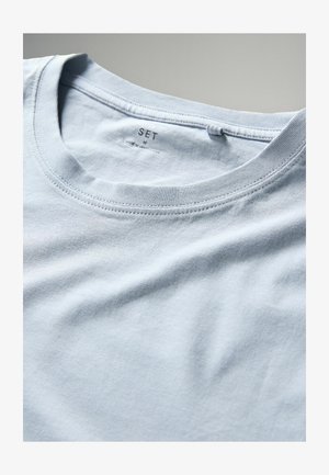 Helles blaues Baumwoll-T-Shirt mit Rundhalsausschnitt, ausgestattet mit einem Etikett mit "SET" und Größe "M". Weiche Textur und glatte Stoffoberfläche.