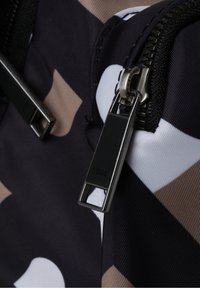 Tissu noir et beige à motif avec une fermeture éclair en métal argenté. La tirette de la fermeture éclair présente une forme rectangulaire, avec le nom de la marque embossé dessus.