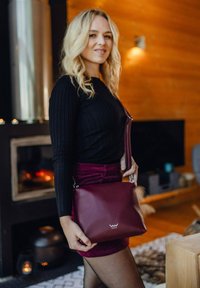 Burgundská kožená kabelka se stříbrnými detaily a logem. Hladký povrch, obdélníkový tvar a nastavitelný popruh.