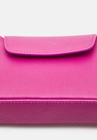 Portafoglio in pelle fucsia con chiusura a soffietto e cuciture visibili su uno sfondo bianco semplice.