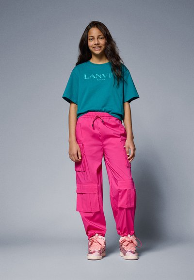 Teal oversized t-shirt with "LANVIN" text, paired with pink cargo pants featuring multiple pockets and elastic cuffs, accented with pink sneakers.