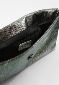 Sac à main texturé vert métallisé avec un motif en cuir de serpent. L'intérieur est en tissu noir, comportant un petit patch logo et une fermeture magnétique.