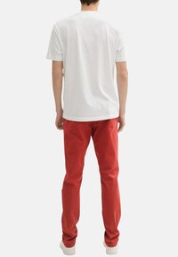 T-shirt en coton blanc à manches courtes, associé à un pantalon en coton rouge. Des baskets blanches complètent la tenue. Vue de dos.