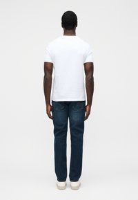 Tricou alb din bumbac, cu decolteu rotund, asortat cu blugi din denim albastru închis, cu buzunare la spate. Model purtând adidași albi.