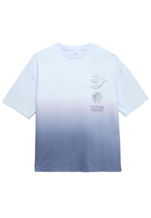 Dreng iført en gradient blå og hvid T-shirt med fugle- og bølgemønstre, lyseblå jeans og brune slip-on sko, stående med armene let ude.