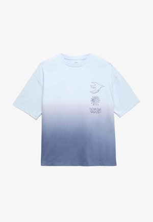 Dreng iført en gradient blå og hvid T-shirt med fugle- og bølgemønstre, lyseblå jeans og brune slip-on sko, stående med armene let ude.