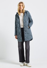 Quiltad blågrå huvjacka med dragkedja fram, sidofickor och texturdetaljer. Matchad med mörka jeans och vita sneakers.