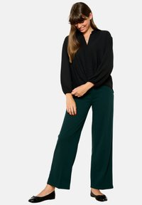 Black button-up blouse with voluminous sleeves, paired with wide-legged green pants and black ballet flats. Simple and relaxed fit.