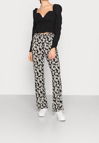 Haut court noir à manches bouffantes avec un décolleté en cœur, associé à un pantalon noir orné d'imprimés marguerites blanches, et des baskets blanches.