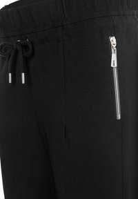 Schwarze Jogginghosen mit Kordelzug in der Taille, ausgestattet mit einer seitlichen Reißverschlusstasche und glattem, strukturiertem Stoff. Akzente aus metallischen Beschlägen.