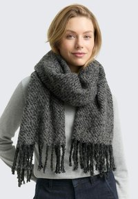 Écharpe en tricot gris avec un motif texturé, aux extrémités frangées et une finition douce, portée sur un haut gris.