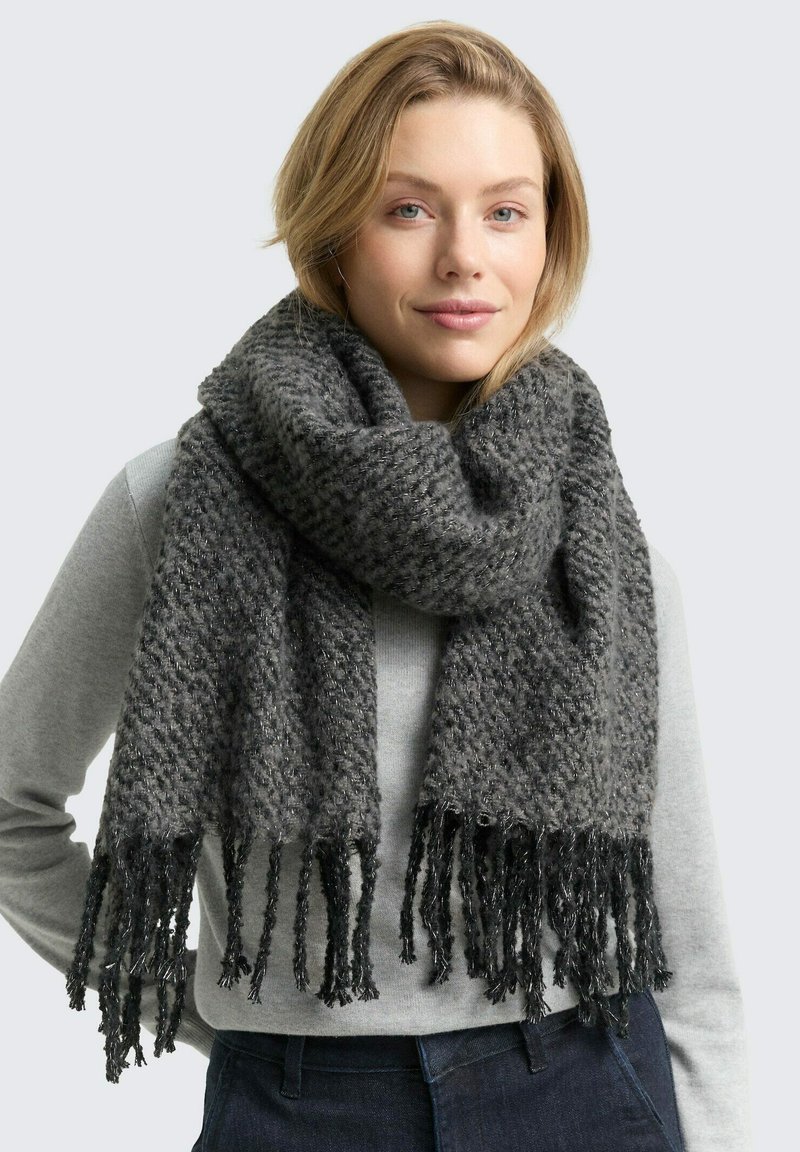 Écharpe en tricot gris avec un motif texturé, aux extrémités frangées et une finition douce, portée sur un haut gris.