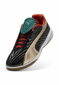 Chaussures de sport avec un dessus noir brillant, des accents dorés et une languette teal. Présente un doublure en maille rouge et une semelle en caoutchouc texturé.