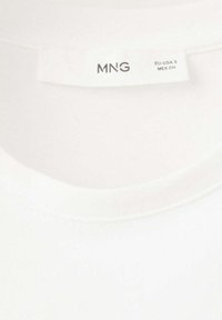 Encolure de T-shirt blanc avec une étiquette de taille indiquant "MNG" et des informations sur la taille EU-USA S, MEX CH.