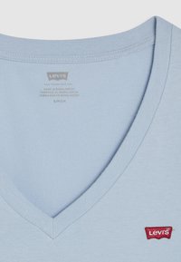Světle modré bavlněné tričko s designem do V a malým červeným logem Levi's na dolní levé straně. Hladká textura.