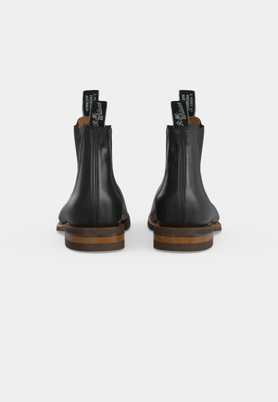 Paire de bottines en cuir noir avec talons marron empilés vues de dos sur un fond blanc uni.