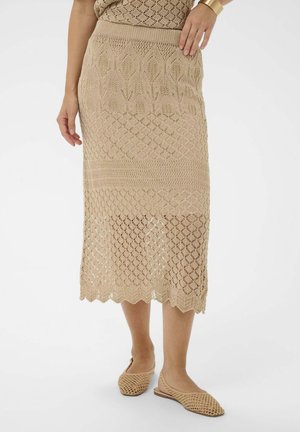 Pletená béžová midi sukňa so zaobleným okrajom, zdobená otvorenými geometrickými vzormi a priliehavým pásom. Nosí sa s béžovými textúrovanými balerínkami v rovnakom odtieni.