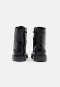 Bottines noires chevauchantes avec une texture croco brillante, des zips à l'arrière et des semelles en caoutchouc robustes. Design simple sans accents supplémentaires.