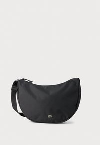 Black fabric crossbody bag with a curved shape, featuring a zip closure and a small green logo on the front. Adjustable shoulder strap.
