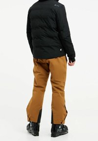 Doudoune noire avec un col haut, associée à un pantalon de neige marron, présentant une jambe fuselée et des accents noirs sur les bottes pour un usage en extérieur.