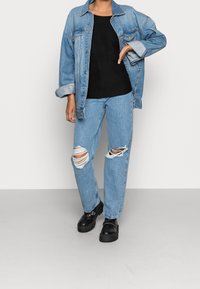 Jasnoniebieska kurtka dżinsowa, czarny podkoszulek z prążkowanej tkaniny, jasnoniebieskie dżinsy z przetarciami i czarne buty na platformie; swobodny, ogólny wygląd.