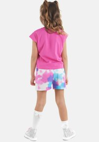 Růžové bavlněné tričko s krátkým rukávem, spárované s šortkami ve stylu tie-dye v modré, růžové a bílé barvě. Bílé ponožky po kolena a stříbrné tenisky dokončují celý outfit.