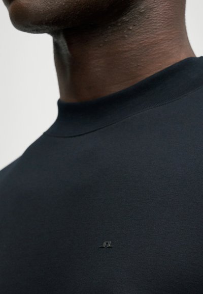 Μαύρη φούτερ μπλούζα με ψηλό λαιμό και κοντούς μανίκους, διαθέτει ένα μικρό λογότυπο κεντημένο στο στήθος σε αντίθετη απόχρωση.