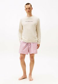 Beżowa koszula z długim rękawem z logo "Tommy Hilfiger", połączona z różowo-białymi, paskowanymi szortami; lekki materiał, casualowy design, luźny krój.
