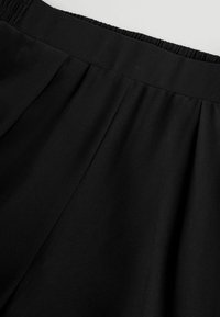 Jupe en tissu noir avec des plis et une ceinture élastique, montrée en gros plan.