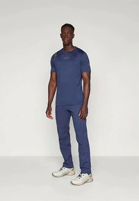 T-shirt atlético azul marinho com textura canelada e logótipo no peito, combinado com calças slim-fit a condizer e sapatilhas de corrida em tons neutros.