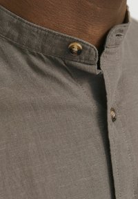 Grey linen collared shirt with a button closure, featuring a textured fabric and visible stitching along the collar and placket.