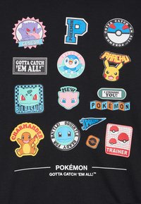 Tessuto nero con toppe a tema Pokémon colorate. Include personaggi come Pikachu, Bulbasaur e elementi di testo in varie forme.
