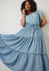 Vestido azul claro, hasta la rodilla, hecho de una tela suave, con un frente abotonado, mangas cortas, cintura elástica y un dobladillo con volantes en capas.