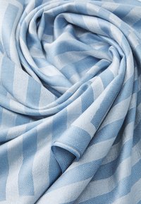 Tissu bleu clair avec un motif pied-de-poule, comportant des nuances variées de bleu. Texture douce avec un aspect drapé, mettant en valeur la brillance du tissu.