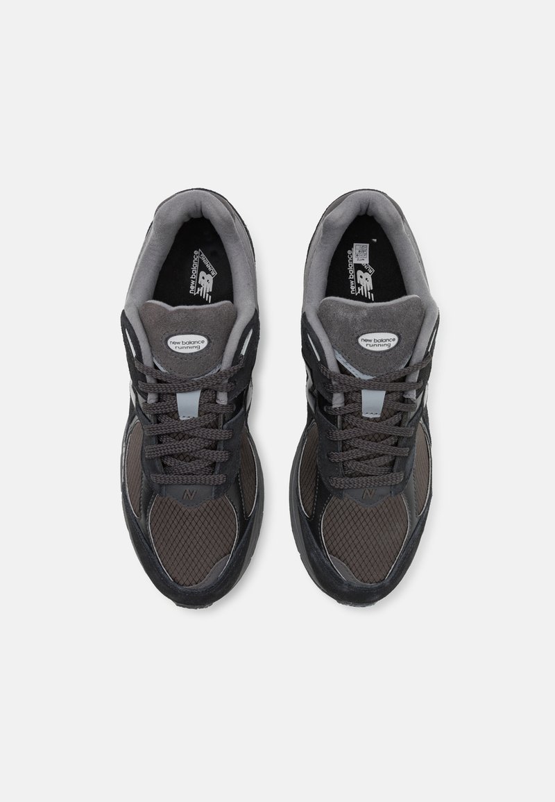 Grijze sportschoenen met gaas- en suèdepanelen, voorzien van donkere veters, een gevoerde tong en een opvallend logo op de bovenkant.