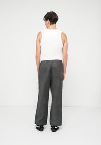 Calças largas cinzentas com um acabamento texturizado, com uma cinta elástica e bolsos laterais, combinadas com uma blusa sem mangas branca simples e sapatos pretos.