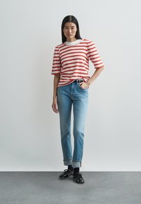 Red and white striped ribbed t-shirt, short sleeves, paired with light blue jeans, featuring cuffs. Black shoes complete the outfit.